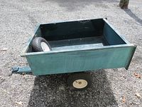 Front and side angle view of the green metal dump trailer with hitch and flat tire visible
