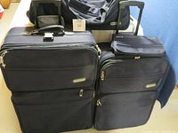 Photo showing two large dark fabric Jetliner suitcases with telescoping handles and wheels, standing upright side by side, with a small toiletry case on top of the smaller suitcase.