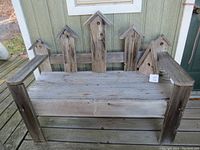 Front view of the rustic barnboard bench showing five birdhouse-shaped vertical backrest panels and thick plank seat and arms.