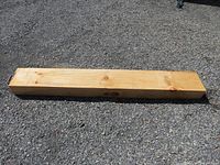 Pine wood beam lying on gravel surface, showing top and side view with natural wood grain visible