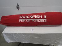 Red carrying bag of the QuickFish 3 Pop-Up Portable Ice Hut with visible brand and product name on the outside.