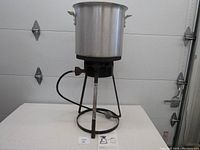 Portable gas stove with circular burner and metal legs connected to a gas hose, some rust visible on legs and burner.