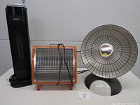 Three portable heaters including a black tower heater, orange framed heater, and round HeatDish heater.