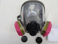 Front view of the 3M respirator showing two pink cartridge filters attached to left and right sides, black face shield with protective cover, and head straps.