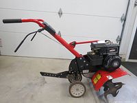 Side view showing red frame, tines, wheels and handle with engine mounted on frame