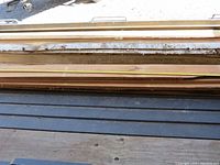 Stack of several rough sawn lumber pieces with a measuring tape laid across showing width in inches, birch and cherry boards visible with natural edges and rough texture.