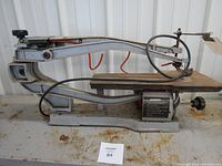 Side view of Busy Bee scroll saw showing metal frame, arm, and worktable with surface rust.