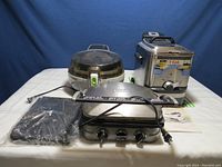 Full view of the three kitchen appliances on a white surface against blue backdrop showing the T-Fal ActiFry, Cuisinart Griddler, and T-Fal deep fryer together.
