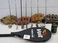 Photo showing the four left-handed ball gloves behind a row of multiple golf clubs, with a Voit black tennis racquet cover in foreground.
