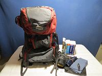 Full view of red and gray Gregory Palisade backpack with open compartments, sleeping bag liner, quick dry towel, and travel books arranged on white surface.