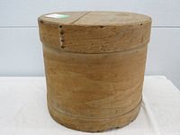 View of the round wooden cheese box showing side and top lid, with visible signs of vintage wear and natural wood grain.