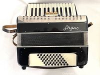 Front view of black and cream Argus piano accordion showing metal grille and bass buttons