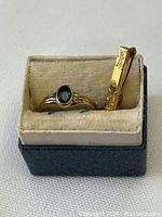 Close-up photo of the baby ring with an oval dark stone and the engraved gold-toned bar pin displayed in a vintage box.