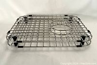 Top view of one stainless steel sink grid showing circular hole and black rubber bumpers.