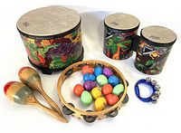 Photo of floor tom, bongos, pair of wooden maracas, tambourine, and colorful plastic egg shakers laid out on a white background.