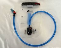 Top view of hydration reservoir showing volume markings, foldover top closure in black and red, and blue detachable hose with red toggle valve and blue bite valve mouthpiece.