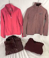 Four women's jackets and sweaters laid out showing varying pink to maroon colors and styles.