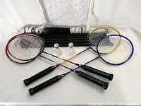 Four badminton racquets laid out with two white shuttlecocks and folded net with poles.