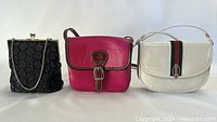 Front view of three purses: black beaded purse, pink leather purse, white leather purse.