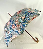 Full view of large floral umbrella featuring a blue background with multicolor floral design and wooden handle.