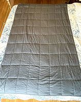 Full view of dark gray weighted blanket laid flat on bed showing square pocket stitch design.
