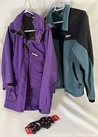 Purple Taiga Goretex parka and green-black MEC coat hanging on white hangers with Life-Sports snow cleats below