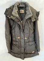 Front view of dark insulated women's winter coat with hood, showing zipped front and pockets.