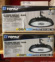 Two unopened boxes of Topaz LED round high bay light fixtures stacked with the front label visible showing product details.