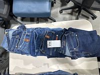 Seven pairs of women's petite 7 For All Mankind vintage jeans stacked on a table showing different blue denim colors and textures with front and back pockets visible.
