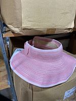 Pink sun visor hat placed on cardboard box, showing woven material and wide brim structure.