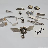 Full assortment of cufflinks and tie clips displayed on white background with lot number