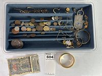 Tray with multiple compartments holding mixed foreign coins and jewelry along top row; banknote and gold-tone bangle placed alongside tray.