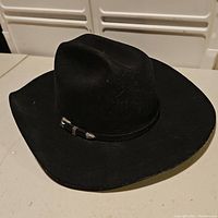 Black Resistol cowboy hat with wide brim and silver accents on band, displayed on white surface with background lockers.