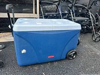 Blue Rubbermaid cooler with light gray lid and wheels seen from front side showing minor scuff mark.