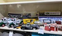 Shelf with various Hess trucks, M-K-T boxcar, black pickup toy truck, Firestone building set, and Hot Wheels car