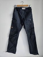 Full front view of black Fjällräven Vidda Pro Ventilated pants hung on hanger against white background showing multiple pockets and button details.
