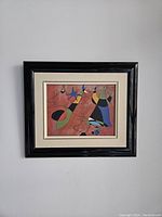 Framed painting showing abstract colorful and geometric shapes with black outlines on a textured red background.