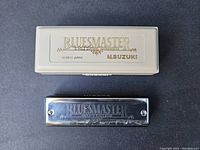 Top view of Bluesmaster harmonica and its off-white plastic case with gold embossing.