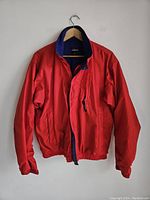 Full view of the red Patagonia jacket hanging showing front pocket details and elastic waistband and cuffs.