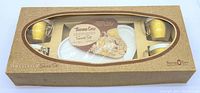 Boxed set showing four gold cups and four white trays inside original packaging with viewing window.