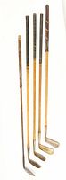 Five antique golf clubs shown side by side with wooden shafts and metal heads, varied grip styles.