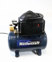 Front and side view of the small air compressor showing the blue tank labeled 'Mastercraft' and the black motor housing with visible switch.