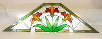 Full front view of triangular stained glass window panel showing vibrant floral design with green border.