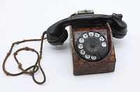 Front view showing the rotary dial with numbers and letters, black Bakelite handset resting on top, connected by cloth-covered cord.