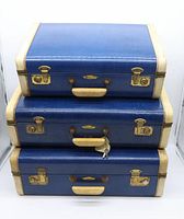 Front view of stacked three vintage blue suitcases with vellum trim showing hardware and handles.