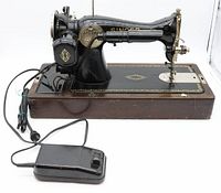 Side view of vintage black enamel Singer sewing machine with decorative gold details mounted on a wood base with foot control connected.
