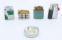 Full view of all five vintage automatic lighters including the green enamelled chrome Penguins, mother of pearl and abalone pigeon lighter, teal leather and brass Buxton lighter, black and chrome Lark 501 lighter, and round mother of pearl and abalone Fisher lighter.