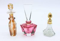 Front angle view of three vintage perfume bottles: amber etched grapevine bottle, pink geometric IMPERLUX bottle, and clear glass with gold-tone dabber stopper.