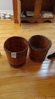 Pair of wooden buckets with metal bands side by side on floor, showing overall size and round open tops.