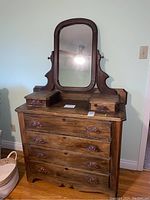Full view of antique wooden dresser with four large bottom drawers and two small top drawers beside attached rectangular mirror with curved top corners.
